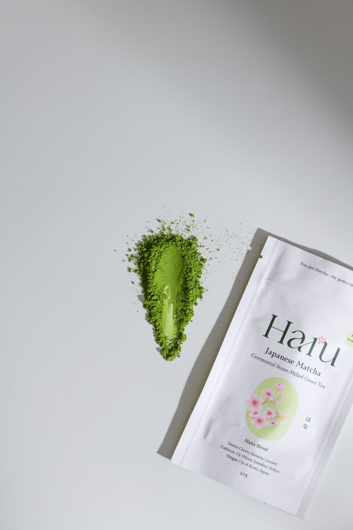 Haru  Hana Japanese Matcha tea package with a scoop of matchaon a light grey background