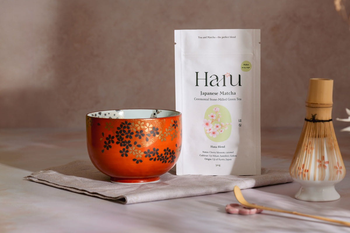 Hanu Hana Japanese Matcha packaging with a traditional orange bowl and whisk on a neutral background