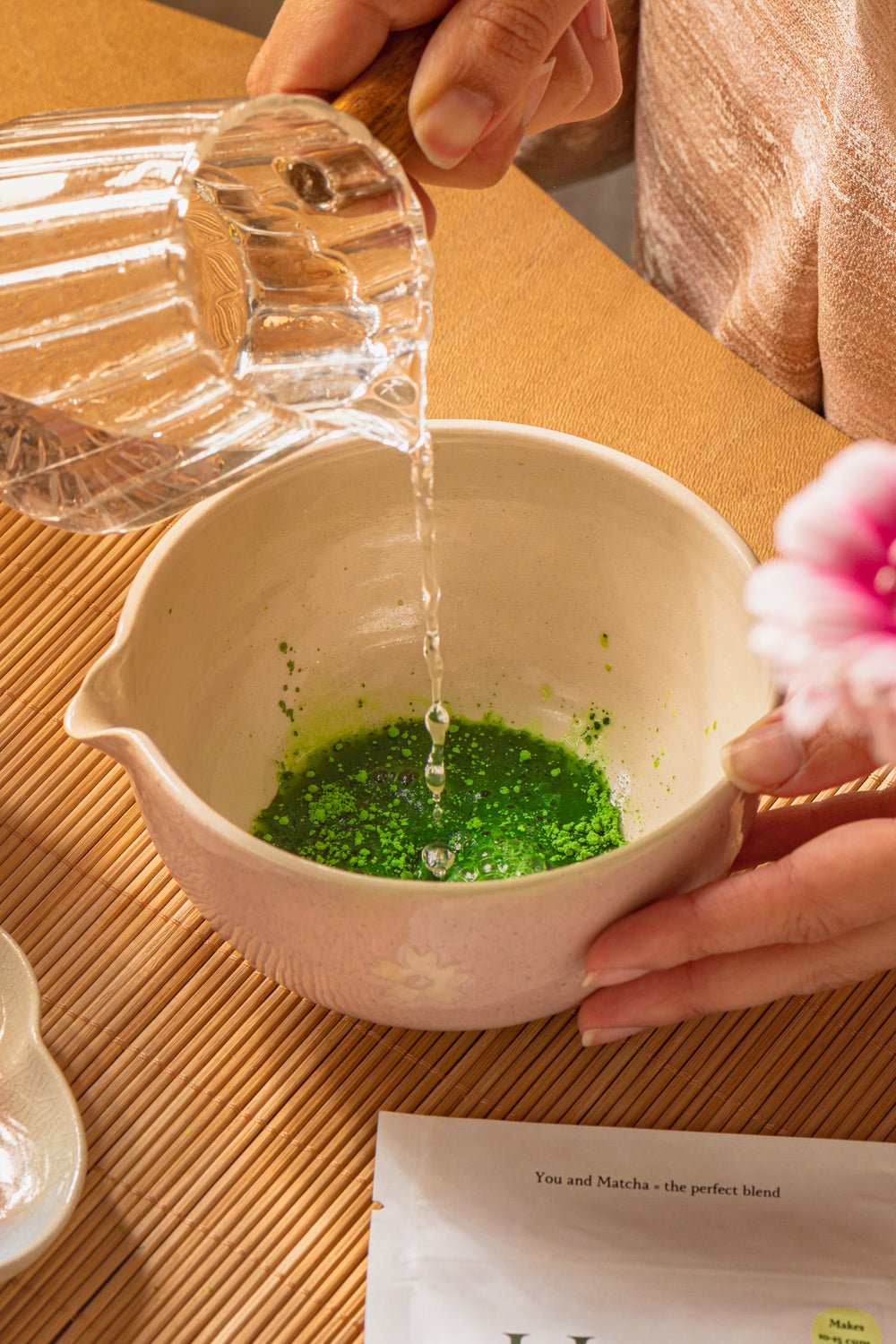 Person pouring water into a bowl with green contents on a wooden table.