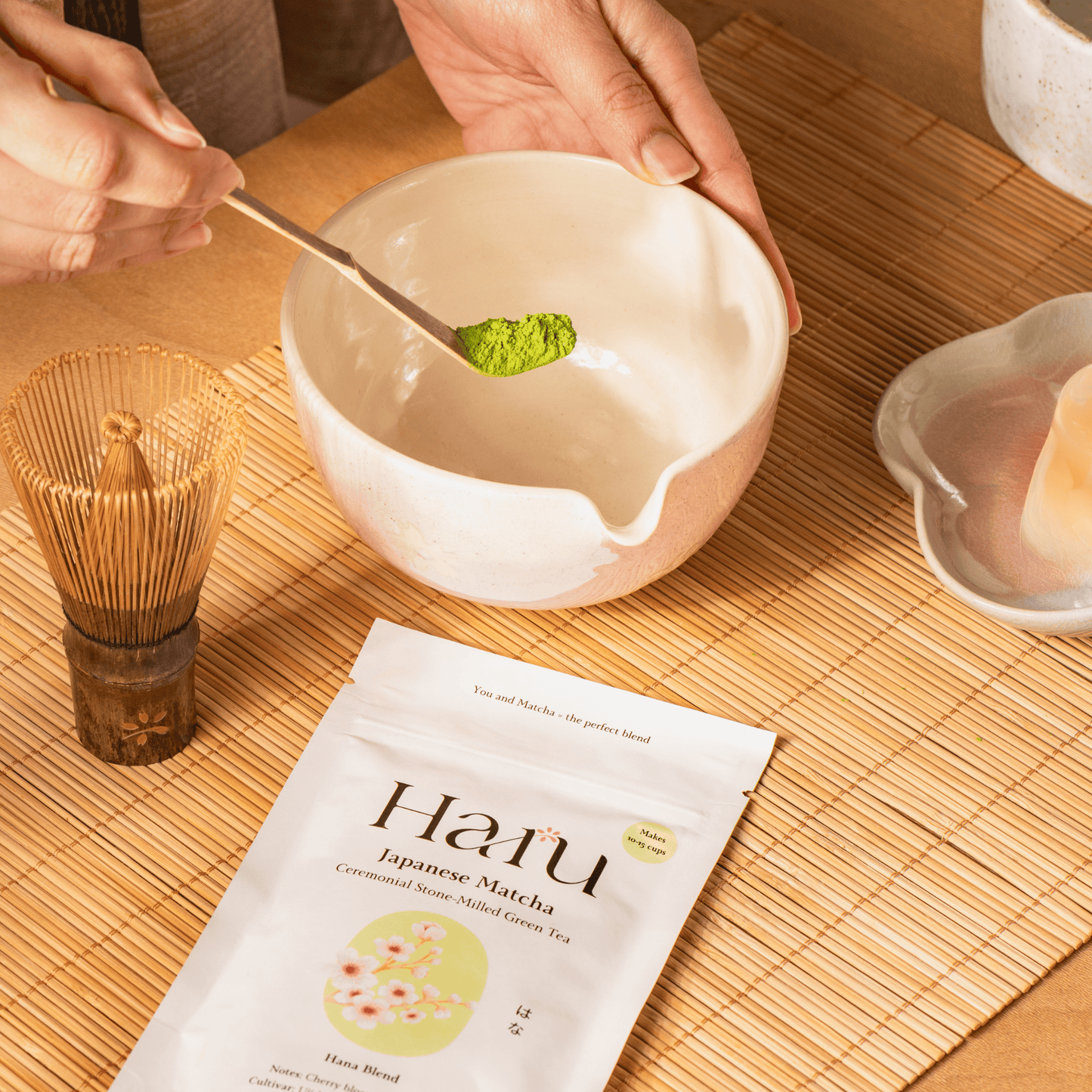 Person preparing matcha tea with a bowl, whisk, and Haru Hana matcha package on a wooden surface.